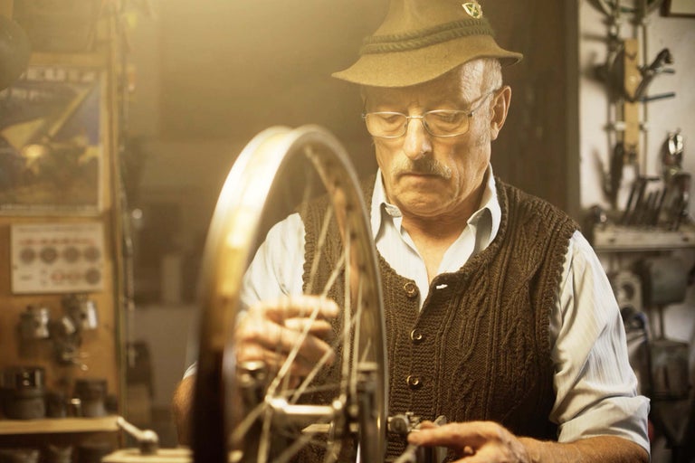 Muž s klobúkom opravuje bicykel v dielni.