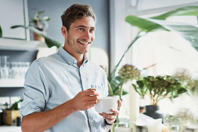 Usmiaty muž s miskou cereálií vo svetlej kuchyni s rastlinami