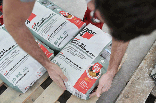 Osoba manipuluje s vrecami záhradného a terénneho betónu na palete