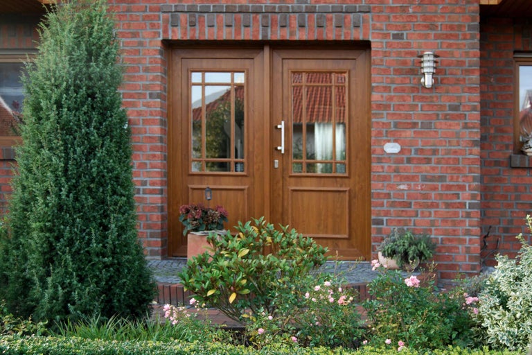 Dvojité drevené dvere so sklenenými výplňami v červenej tehlovej fasáde obklopené rastlinami