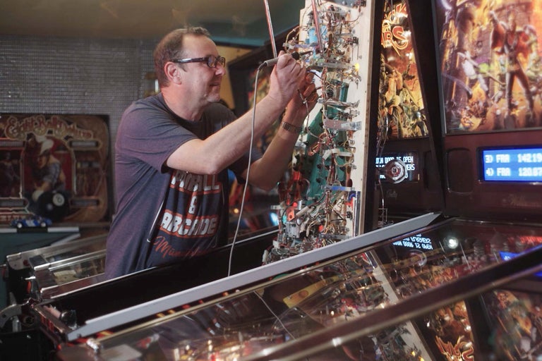 Muž opravuje pinballový automat.