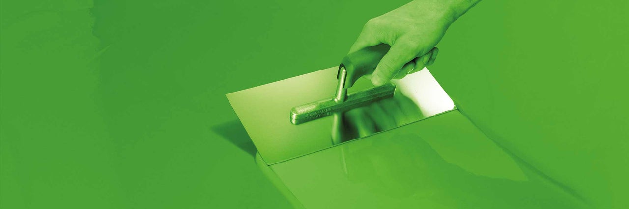 Ruka drží hladidlo pri nanášaní poteru.