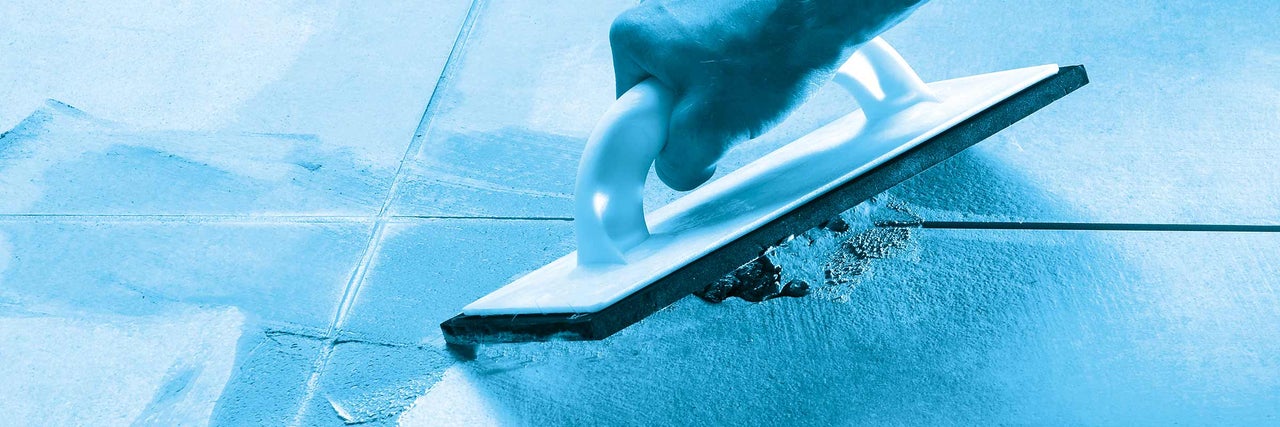 Ruka s gumovou stierkou pri škárovaní dlaždíc