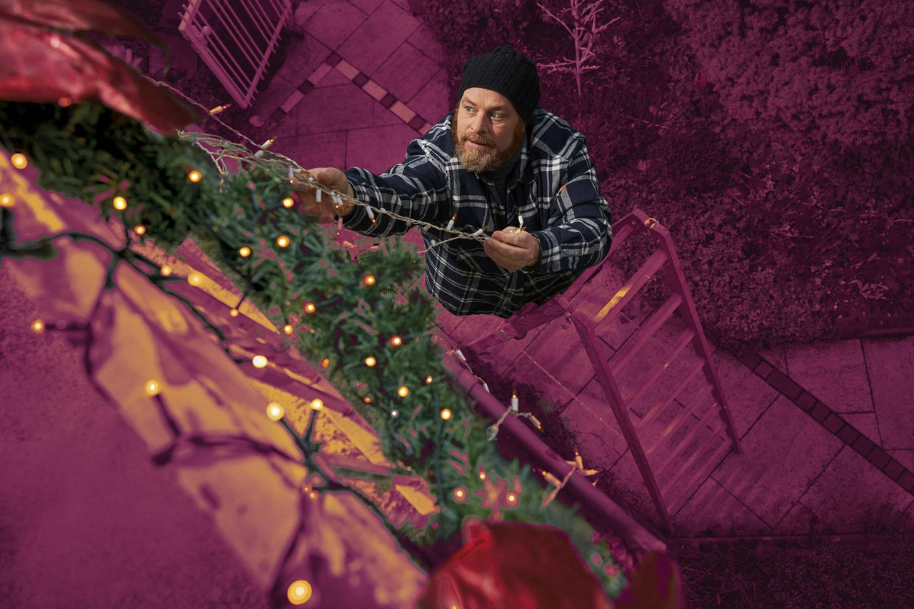 Muž zdobí strechu svetelnou reťazou z rebríka