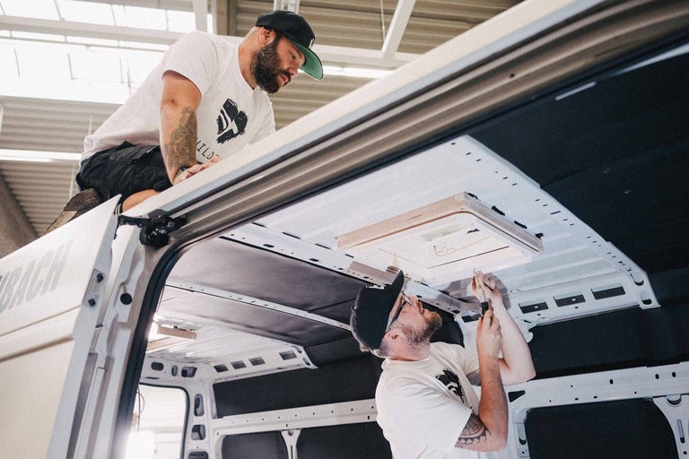 Dvaja remeselníci inštalujú strešné okno do dodávky.