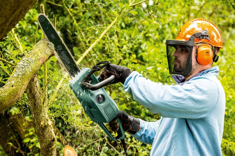 Muž s ochrannou prilbou pracuje s reťazovou pílou Bosch na strome.