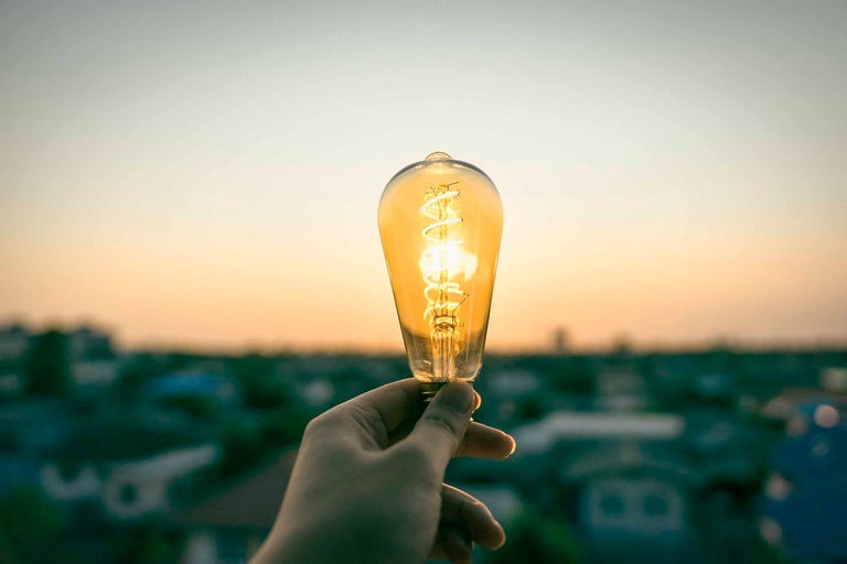 Ruka drží žiarovku s vláknom pred rozmazaným pozadím.