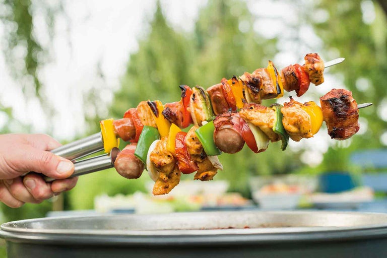 Dve špízy s mäsom a zeleninou držané nad grilom.