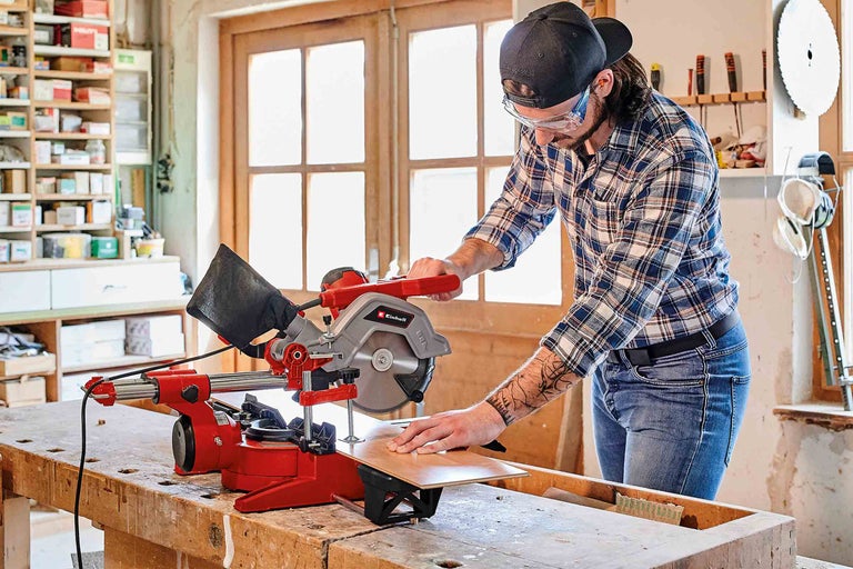 Muž reže drevo pokosovou píl Einhell v dielni.