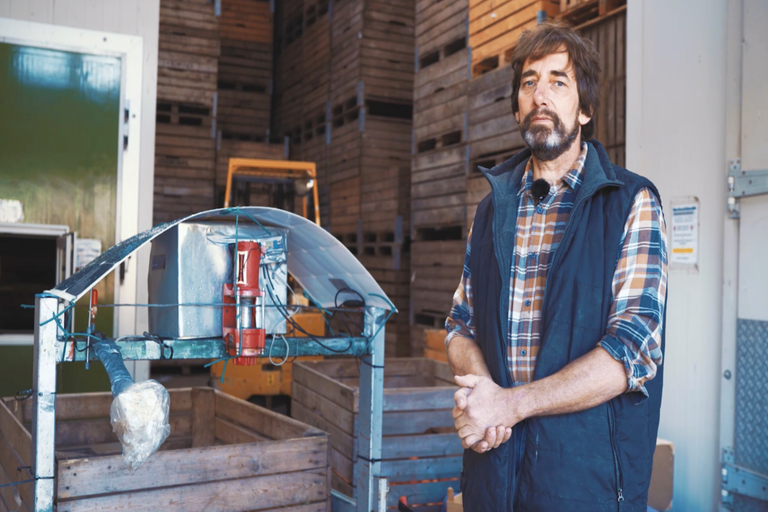 Muž stojí vedľa drevených kontajnerov a vysokozdvižného vozíka v sklade