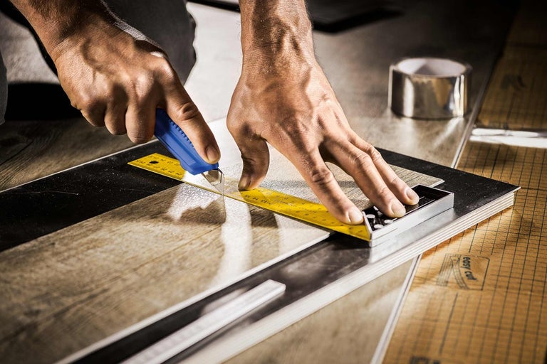 Muž reže vinylovú podlahovú dosku rezačkou a uholníkom.