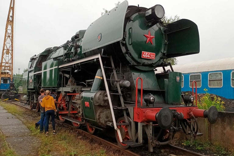 Zelená parná lokomotíva s červenou hviezdou a číslom 464 202 stojí na odstavnej koľaji.