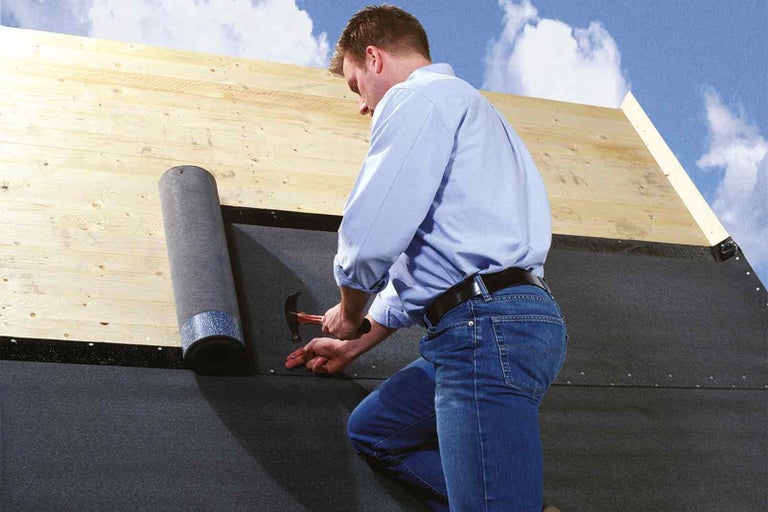 Muž pripevňuje strešnú fóliu kladivom na strechu.