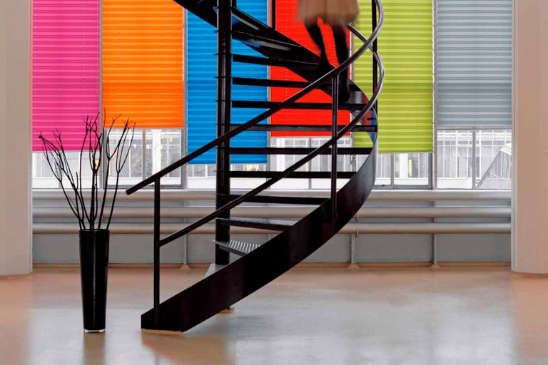 Interiérová fotografia so špirálovým schodiskom a rôznymi plisovanými žalúziami pred oknami