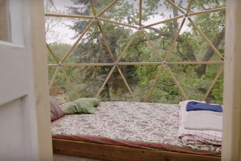 Interiér dreveného kupolového domu s posteľou a výhľadom na stromy