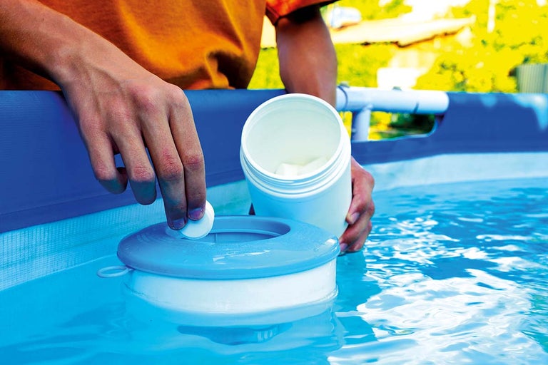Osoba vkladá chlórovú tabletu do plaváka dávkovača bazénovej chémie