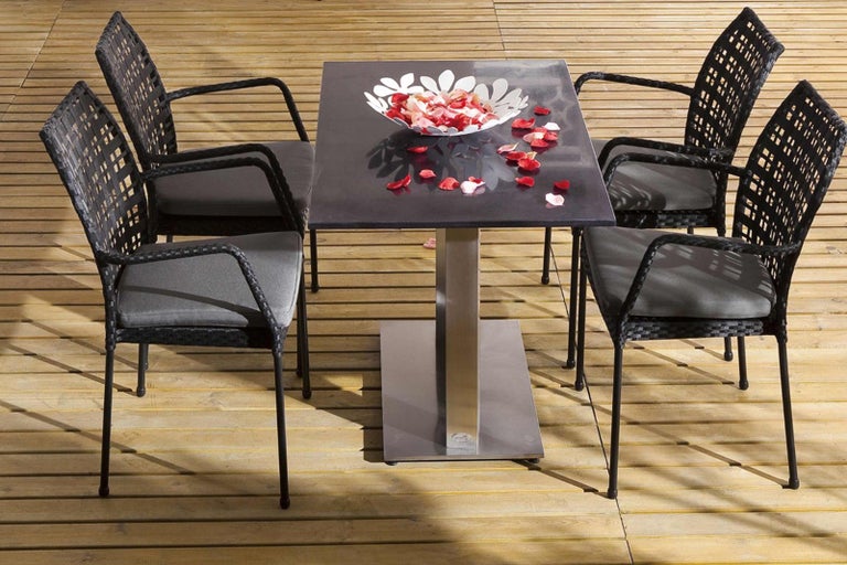 Štvorcový záhradný stôl so štyrmi ratanovými kreslami a dekoráciou na drevenej terase