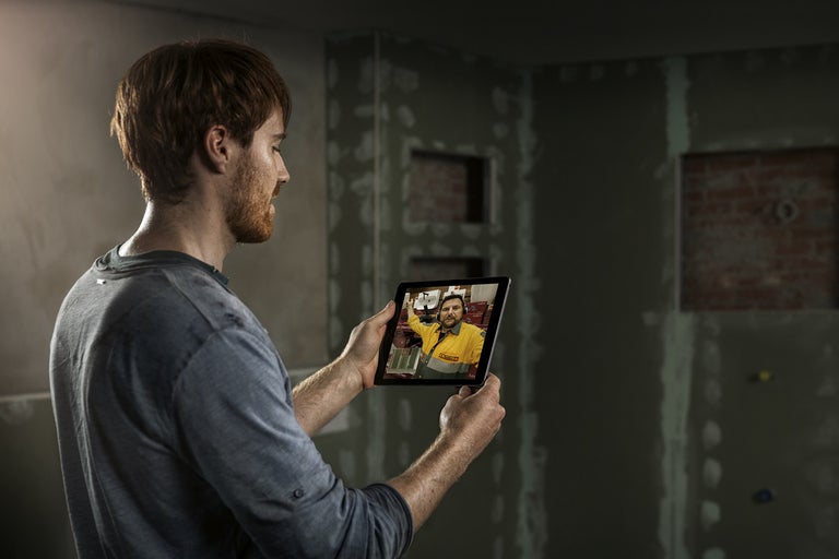 Muž drží tablet s videoporadenstvom pred stenou vo výstavbe.