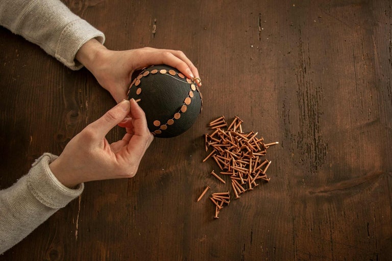 Ruky zdobia čiernu guľu klincami na drevenom stole.