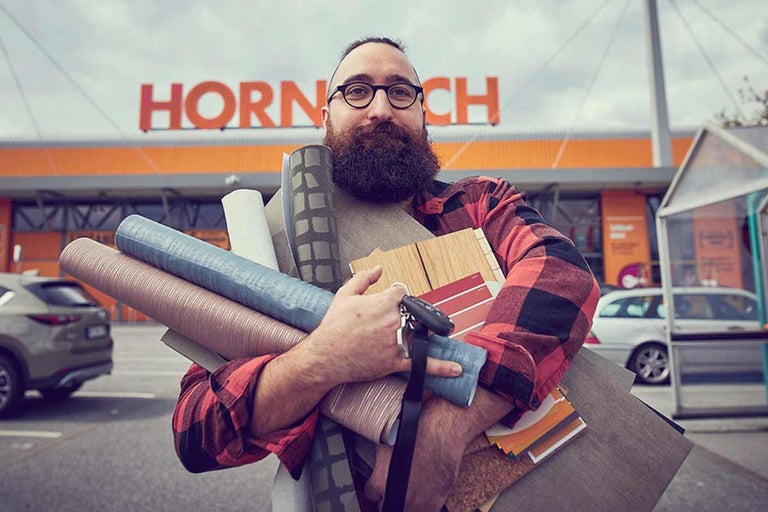 Muž pred predajňou Hornbach nesie rôzne stavebné materiály.