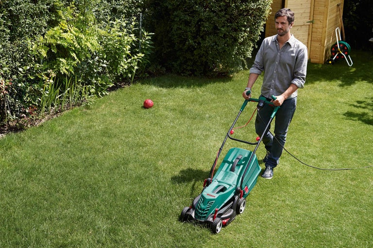 Muž kosí trávnik elektrickou kosačkou na záhrade.