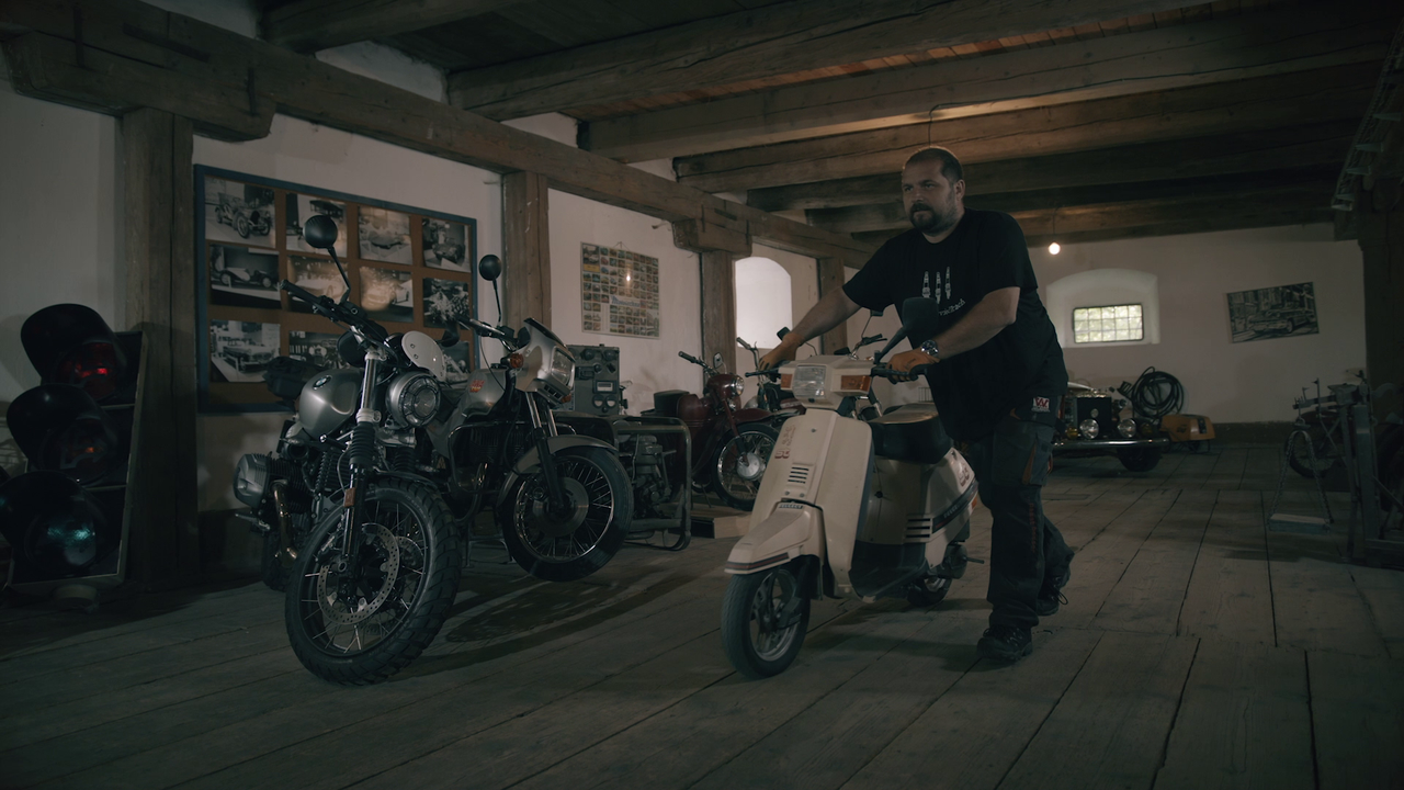 Muž tlačí skúter v garáži s niekoľkými motocyklami
