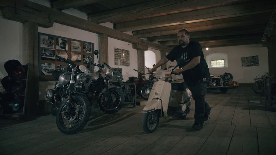Muž tlačí skúter v garáži s niekoľkými motocyklami