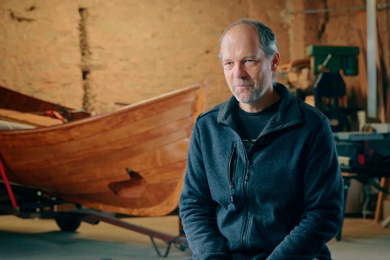 Muž pred drevenou loďou v dielni