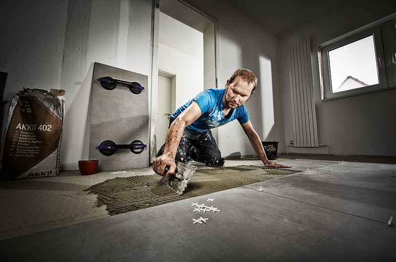 Dlaždič pracuje vo svetlej miestnosti s dlaždicami, lepidlom na dlaždice, rezačkou dlaždíc a náradím