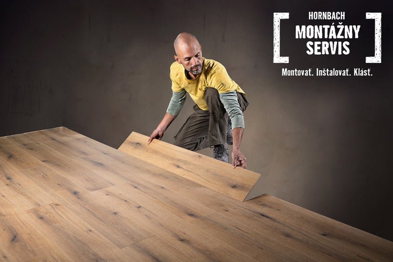 Muž pokladá drevené parkety v miestnosti, montážny servis Hornbach.