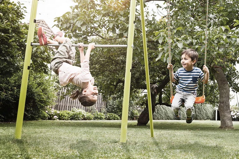 Deti sa hrajú na záhradnej zostave s hojdačkou a hrazdou v záhrade.