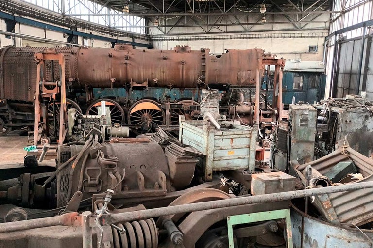 Stará lokomotíva a strojové súčasti v továrenskej hale.