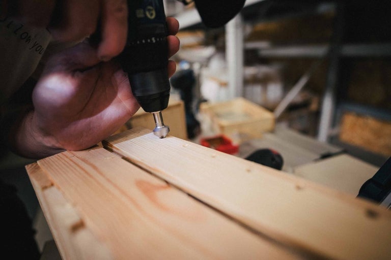 Osoba zapúšťa skrutky do drevenej dosky pomocou skrutkovača.