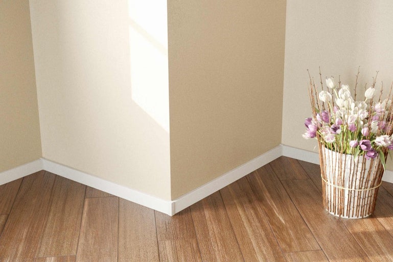 Roh miestnosti s drevenou podlahou, bielymi podlahovými lištami a kvetinovou väzbou v pletenom košíku