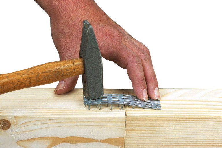 Remeselník pripevňuje klincovú dosku ku dvom kusom dreva kladivom.