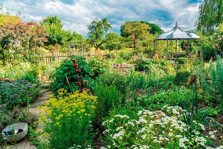 Bujná záhrada s kvetmi, rastlinami a záhradným altánkom