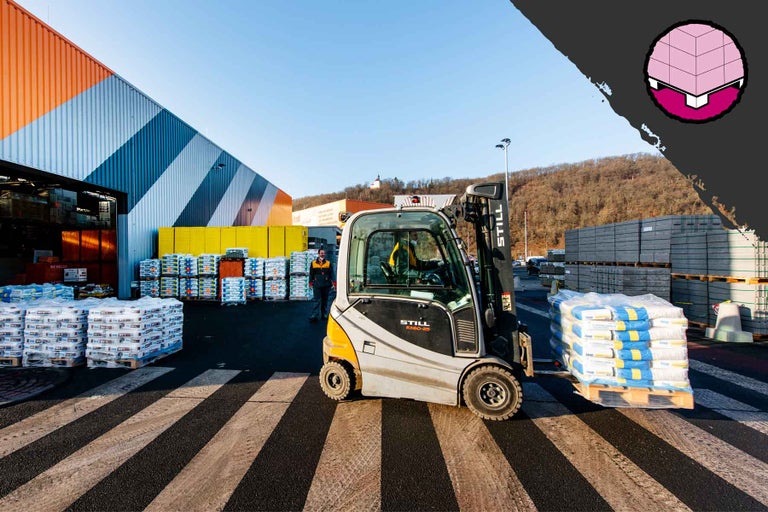 Vysokozdvižný vozík prepravuje palety so stavebnými materiálmi pred predajňou Hornbach.