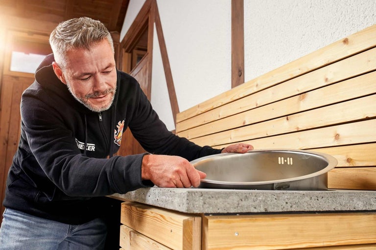 Muž inštaluje drez do záhradnej kuchyne