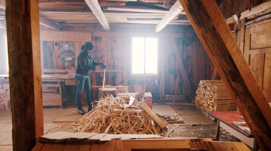 Interiér dielne s drevenými stenami a ženou pracujúcou s drevom.