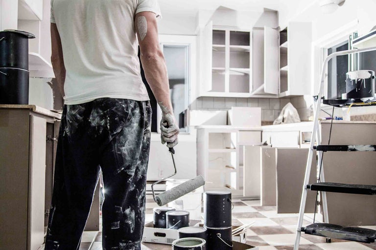 Muž renovuje kuchyňu pomocou valčeka na maľovanie, plechoviek s farbou a rebríka.