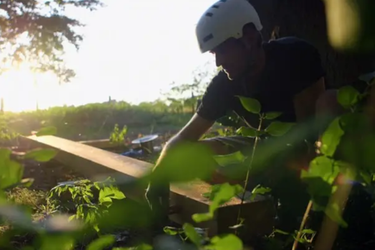 Muž s ochrannou helmou pracuje s drevom v záhrade.