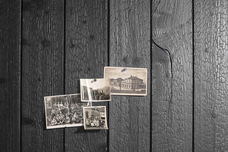 Staré fotografie pripevnené k čiernemu drevenému obloženiu pomocou pripináčikov