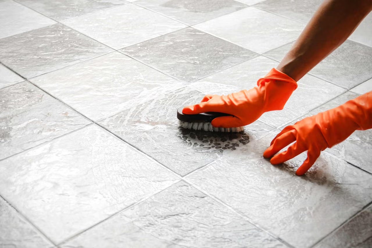 Čistenie podlahových dlaždíc kefou a ochrannými rukavicami