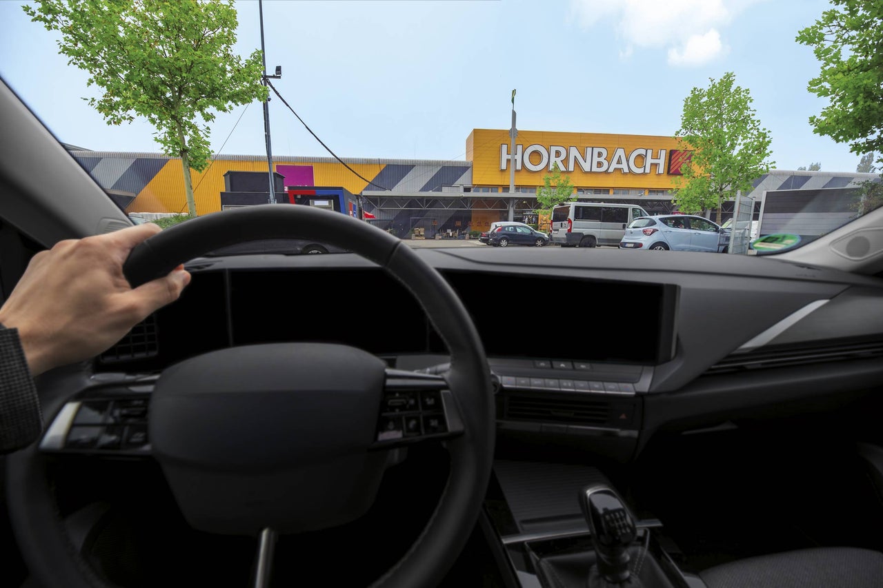 Pohľad z interiéru vozidla na predajňu Hornbach s Hornbach Logo, parkoviskom a stromami.