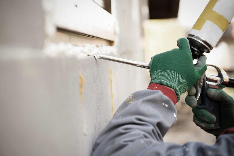 Remeselník utesňuje škáru penovou pištoľou.