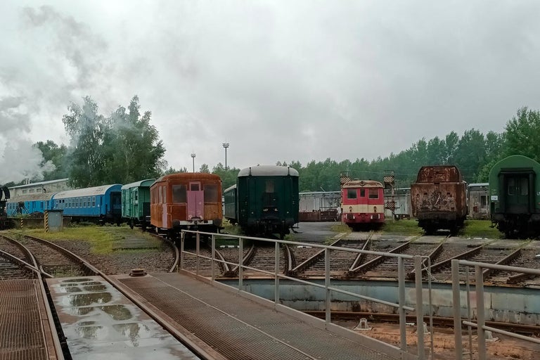 Rad železničných vozňov rôznych typov stojí vonku na koľajniciach.