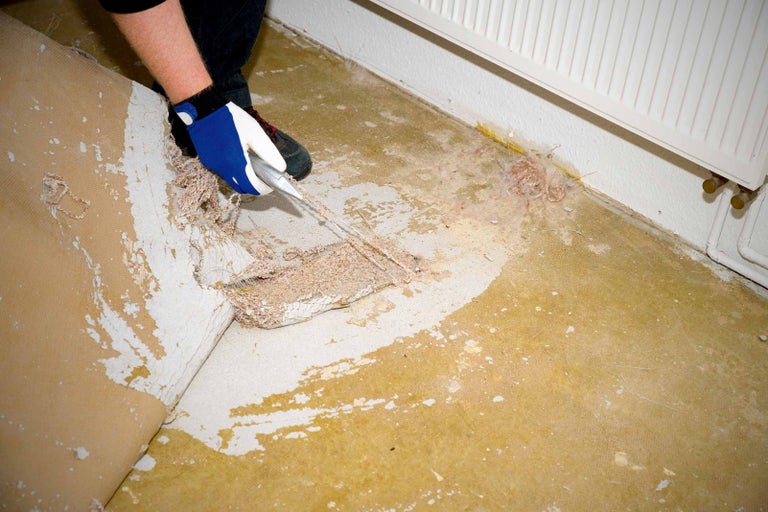 Osoba odstraňuje starú podlahovú krytinu nožom.