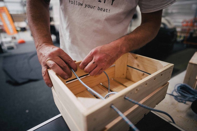 Osoba navlieka šnúru do drevenej bedne.