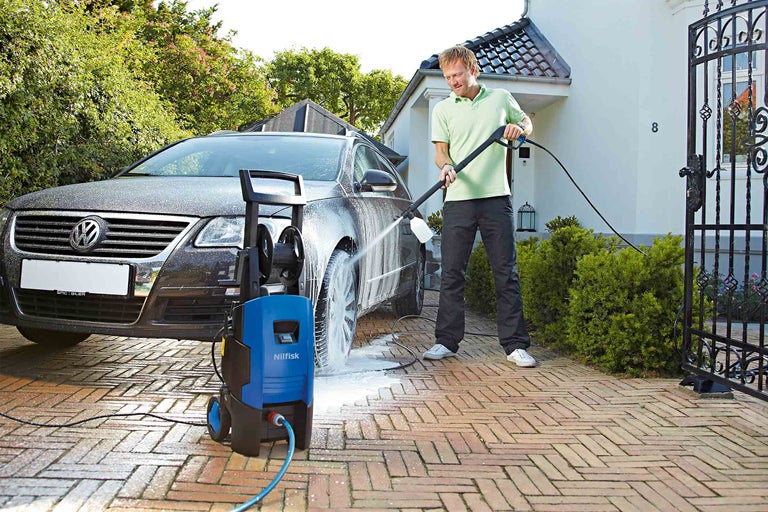 Muž čistí auto vysokotlakovým čističom Nilfisk na príjazdovej ceste.
