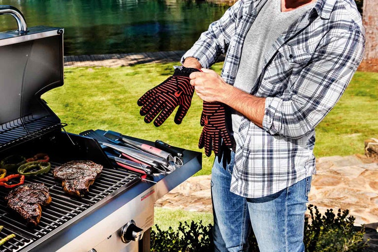 Muž nosí žiaruvzdorné grilovacie rukavice vedľa grilu s mäsom a zeleninou.